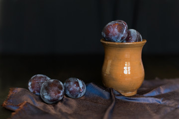 plums on a dark background in a glass vase clay blue summer berry fruits