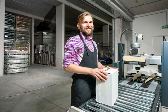 Handsome packer in working apron with box on the packaging line at the manufacture.