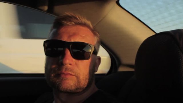 Young casual man with beard portrait sitting on the backseat of car. Urban male hipster in his 30s. Sunset