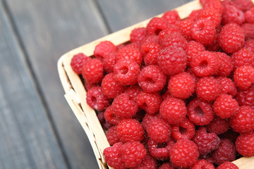 Red fresh raspberries basket on brown rustic wood background