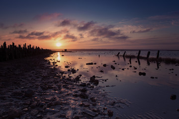 Beautiful sunny red colorful sunset on the lake with stones, wooden posts and reflection, natural seasonal summer vacation background