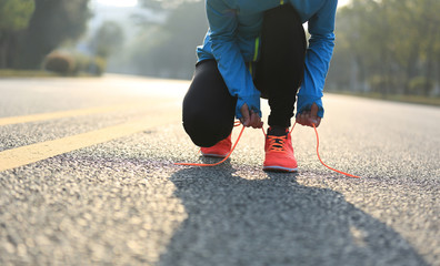 young woman runner tying shoelaces on road