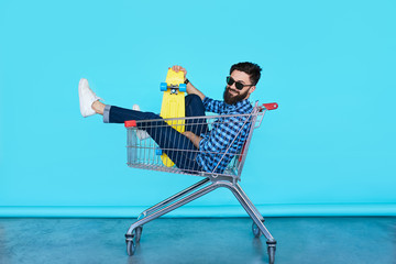 Side view of cheerful young man sitting in shopping cart