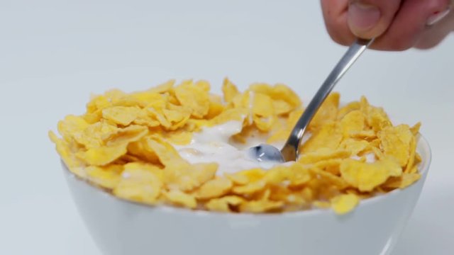Someone is putting a spoon into a cup with corn flakes, blueberries and milk. He is starting to eat his breakfast. Close-up shot.
