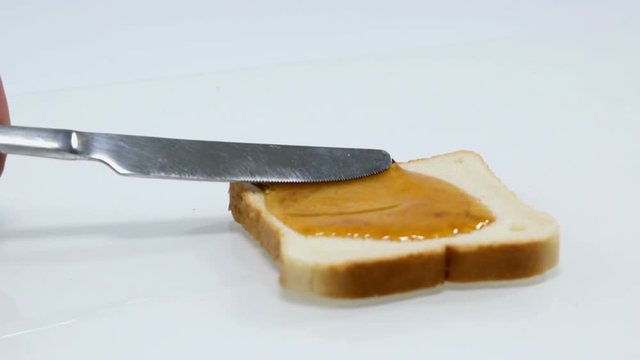 Someone is slowly spreading some honey on a piece of bread with a knife. It looks as a very yummy snack.
