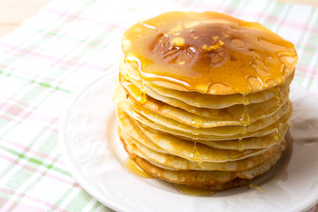 Stack of breakfast pancakes with honey on the white plate