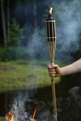 Man hand with torch in wild smoky nature background.
