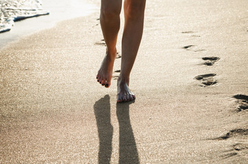 Women's feet are in the sand on the coast