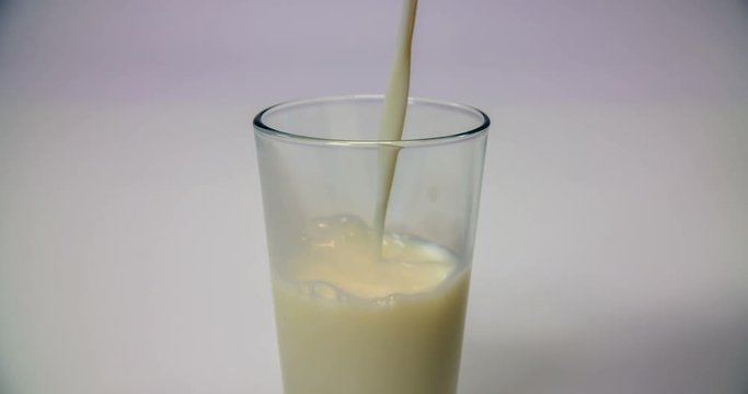 A glass full of vanilla milkshake is standing on a kitchen table for someone to drink it. Close-up shot.
