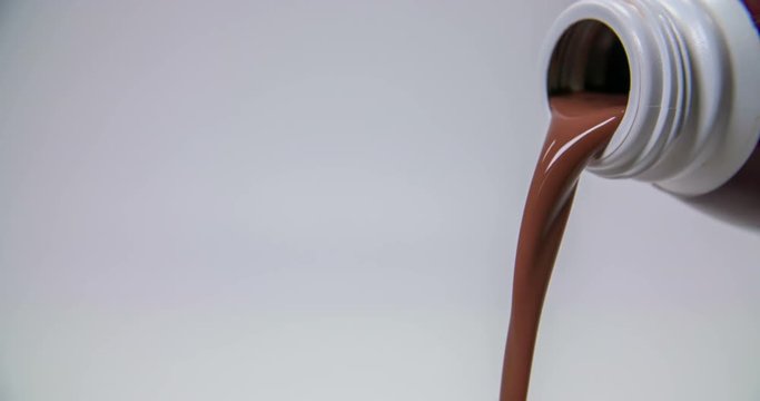 Some chocolate milk is pouring out of a bottle and into a glass which is standing on a table. Close-up shot.
