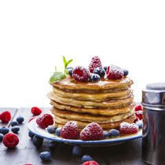 Pancakes with honey and berries on white background