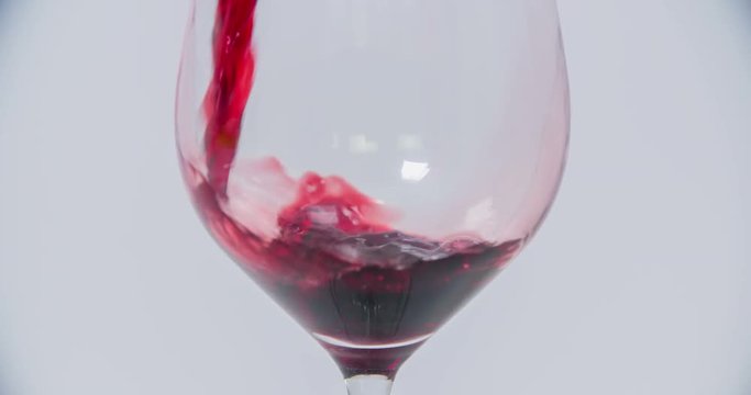 Red wine is pouring into an empty glass that is standing on a table in the kitchen. Close-up shot.
