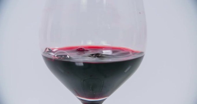 A glass of red wine is standing on a table in the kitchen. It is already half full. More drops od red wine are falling into this glass. Close-up shot.
