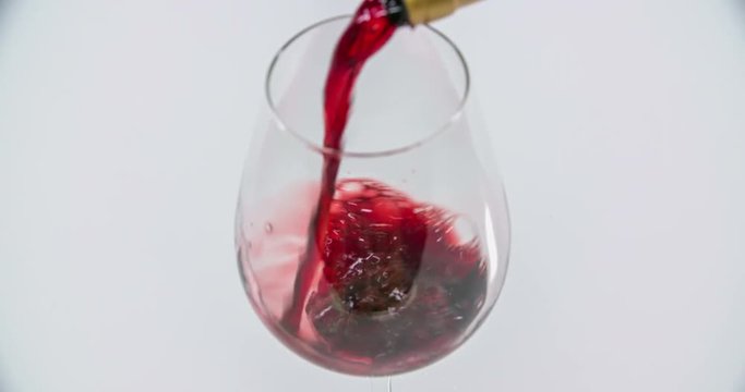 A clean glass is standing on a table in the kitchen and someone starts pouring red wine into it. Close-up shot.

