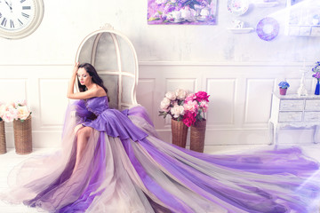 Beautiful brunette woman wearing long purple dress posing in studio interior