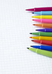 Colorful felt tip pens arranged on a white squared paper background to form a page border