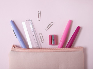 A school pencil case with stationery spilling out on to a pastel pink background - obrazy, fototapety, plakaty
