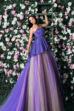 Beautiful brunette woman wearing long purple dress posing in the flowered garden