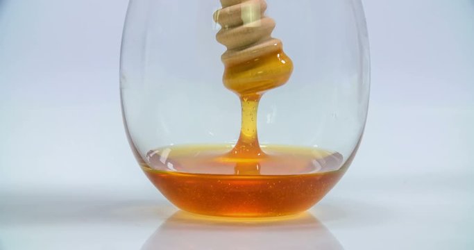 Someone slowly lifts up a wooden honey stick in a glass and the honey starts pouring back down very slowly. Close-up shot.
