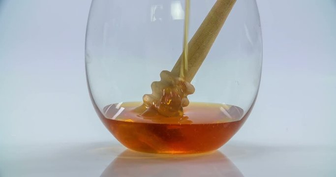 Someone is pouring some honey in a glass and some of it falls on a wooden honey stick. Close-up shot.
