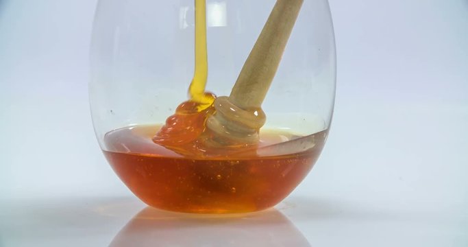 Honey is slowly pouring down into a small glass. There is a wooden honey stick in there too. Close-up shot.
