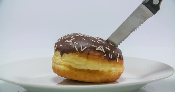Someone is trying to cut a delicious doughnut into a half and the plate lifts up a bit. Close-up shot.
