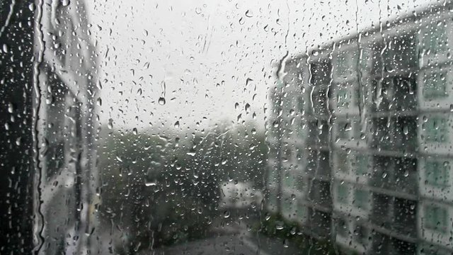 Drops of rain on a window pane, buildings in background.