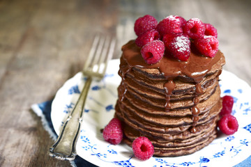 Stack of chocolate pancakes topped with chocolate and fresh rasp