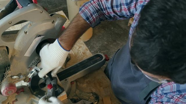 Carpenter works with wooden bar in workshop near electric saw.