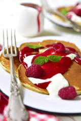 Pancakes with raspberry sauce and cream on a vintage plate.
