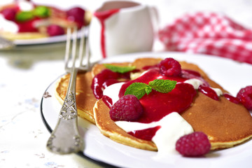 Pancakes with raspberry sauce and cream on a vintage plate.