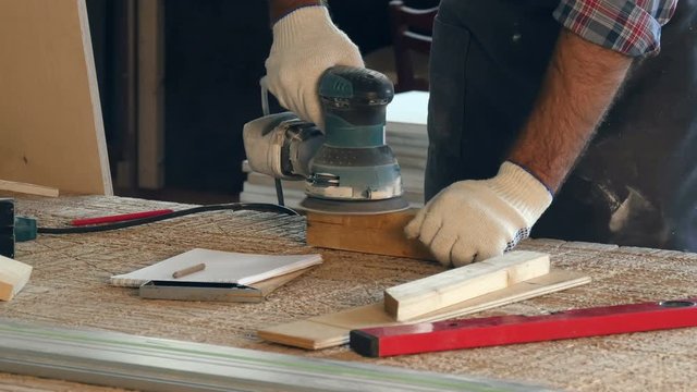 Man working with wooden planck and electric planer write in notebook.