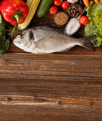 Fresh raw fish with vegetables on old wooden background