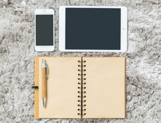 Closeup brown note book , brown pen , tablet and smart phone on gray fabric capet textured background in top view in work concept
