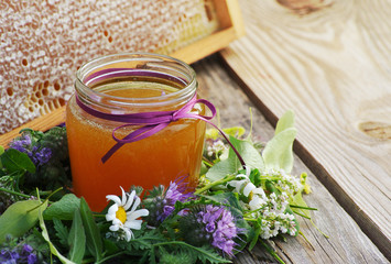 Obraz na płótnie Canvas Honey in a glass jar and bee honeycombs with flowers melliferous herbs on a wooden surface. Honey with flowers.