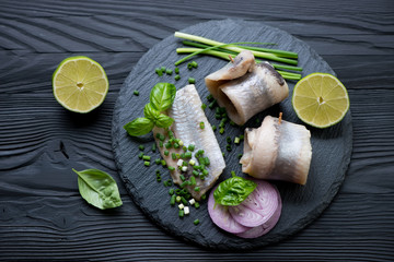 Herring fillet on a stone slate tray, black wooden background