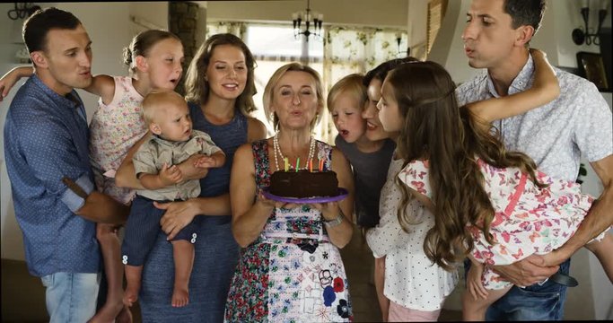 Multi generation family celebrating birthday at home, blowing out candles on birthday cake