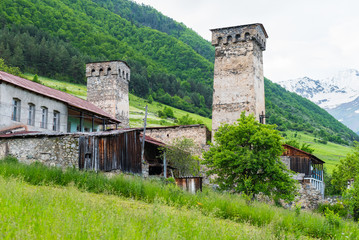 Medieval stone defensive towers of Mestia, Svaneti, Georgia with dwelling houses around and outbuildings. A traditional Svan household. Wooded mountain slope and snow-capped peak behind the scene