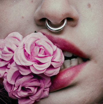 Nariz y boca de una mujer mordiendo unas flores con un piercing en la nariz 