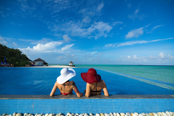 Two women in a hat sitting on the edge of the swimming pool