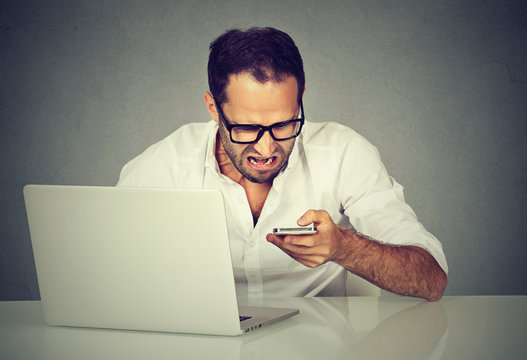 Frustrated man with laptop texting on his mobile phone