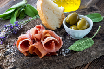 Prosciutto with olives on wooden background