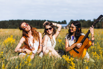 Three cute hippie girl sitting on grass outdoors, best friends having fun and laughing, playing the...