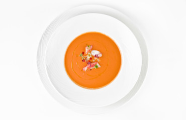 Pumpkin cream soup with cucumbers, tomatoes, shrimp and olive oil on a plate on a white background,...