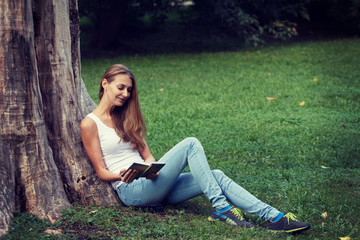 Naklejka na ściany i meble Young woman sitting on the grass and reading book outdoor.