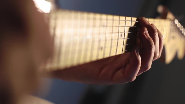 A man playing fast solo on electric guitar in the recording studio neck close-up
