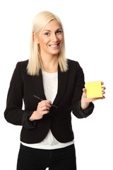 Attractive businesswoman in black suit and white shirt, holding a pad of sticky notes with a pen. White background.