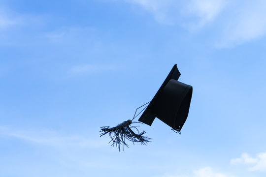 One graduation cap or mortar board thrown up to the air, sky background