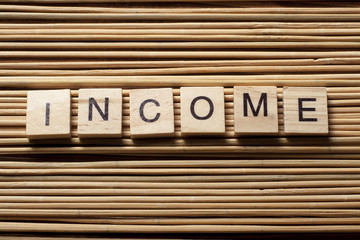 Income word written on wood block at wooden background