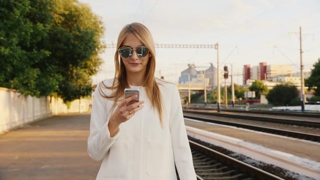 Young woman in sunglasses smiling, talking on the Peron along the railway. use smartphones
